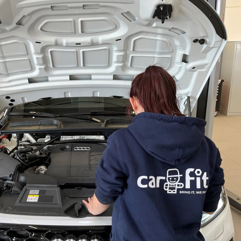 Person wearing a 'car fit' hoodie working on a car engine.