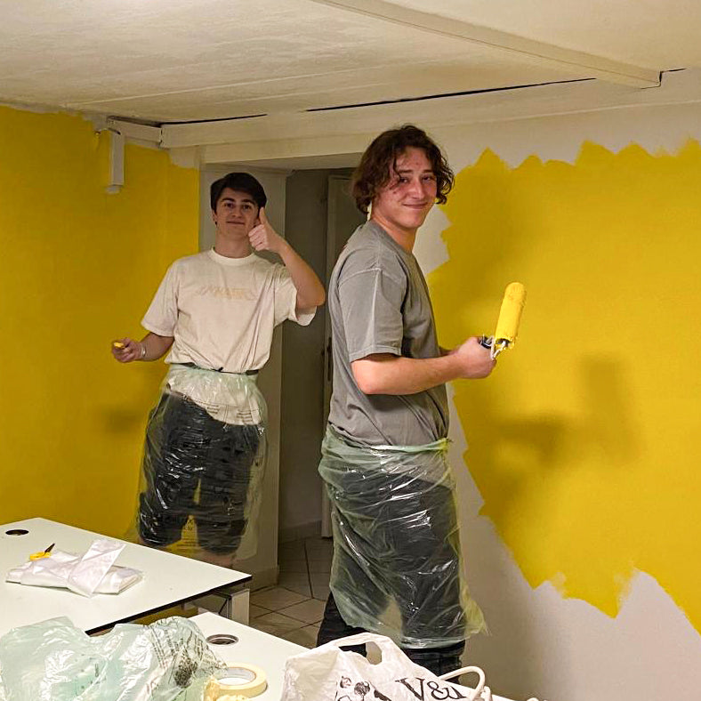 Two people painting a print shop room with yellow walls and white ceiling.