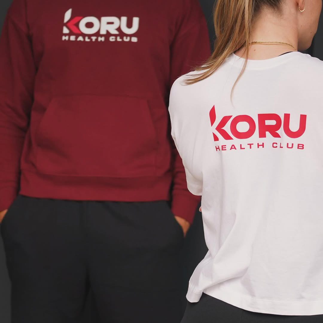 Two people wearing sweatshirts with 'Koru Health Club' logo on the back.