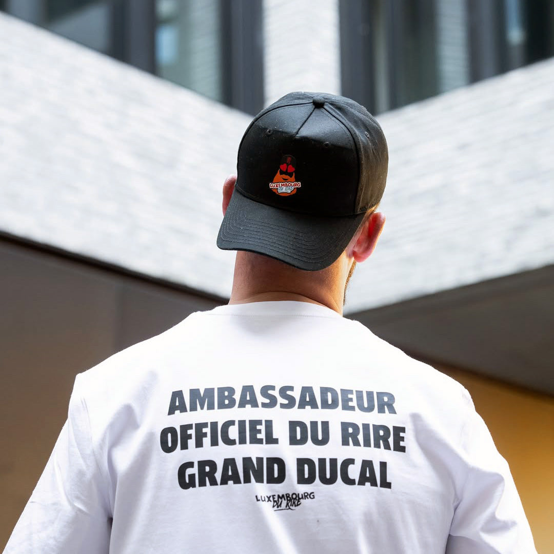Person wearing a black cap and white t-shirt with text, standing in front of modern architectural elements.