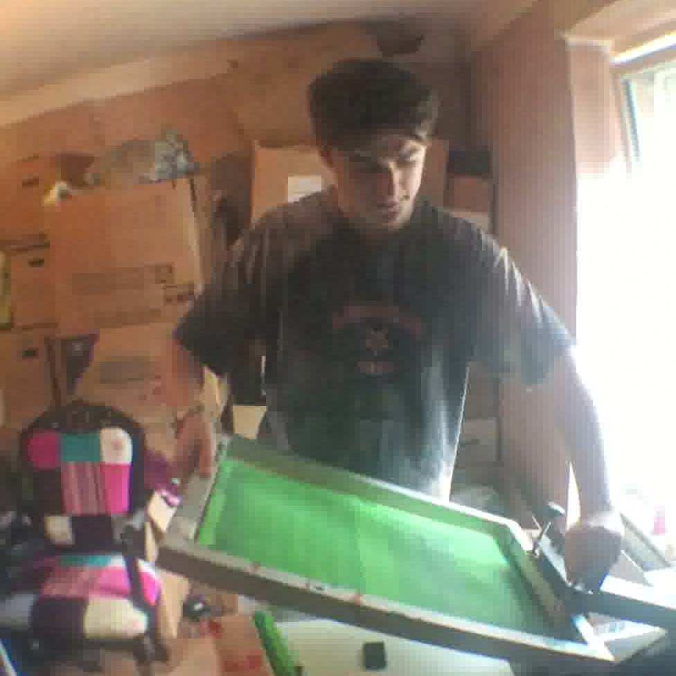 Person working on a screen printing project with a green screen in a room with cardboard boxes.